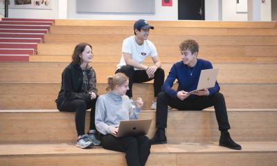 Fire elever fra HHX i Lyngby sidder på en trappe med deres computer og taler sammen